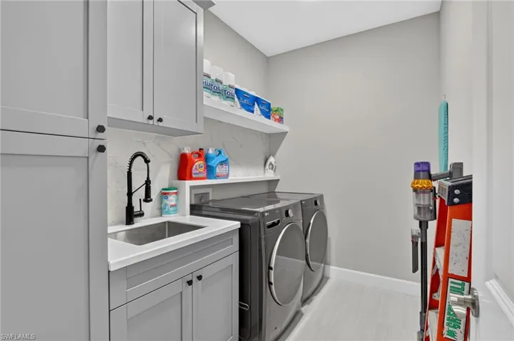 Laundry room featuring light gray cabinetry, a built-in sink with a matte black faucet, white countertops, and a white floating shelf