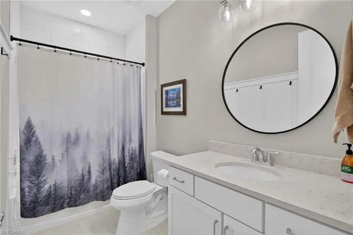 Bathroom featuring a white vanity with a light-toned countertop, an undermount sink, and a circular black-framed mirror