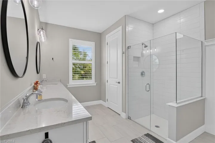 Modern bathroom featuring a dual vanity with undermount sinks and light-toned countertops, a glass-enclosed shower with horizontal tile surround, a window with louvered blinds, and light wood-finish flooring