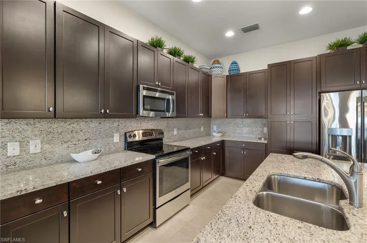 Kitchen with light stone countertops, appliances with stainless steel finishes, dark brown cabinets, and sink