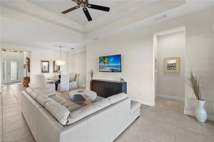 Living room with ceiling fan, light tile patterned flooring, and a tray ceiling