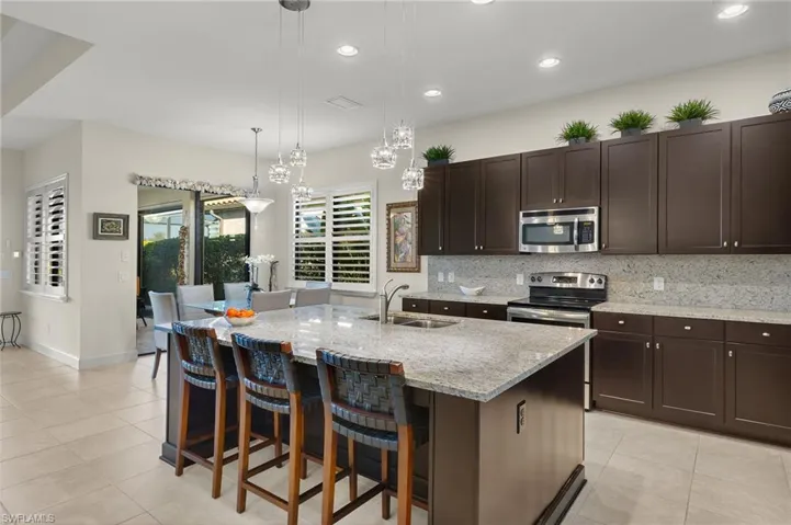 Kitchen with sink, tasteful backsplash, an island with sink, decorative light fixtures, and appliances with stainless steel finishes