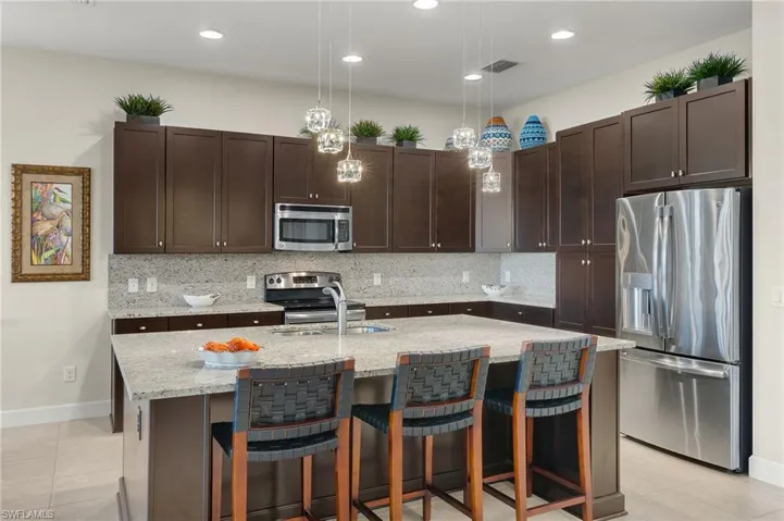 Kitchen with a center island with sink, hanging light fixtures, decorative backsplash, appliances with stainless steel finishes, and dark brown cabinets