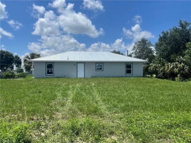 Back of property featuring stucco siding, a lawn, and a metal roof