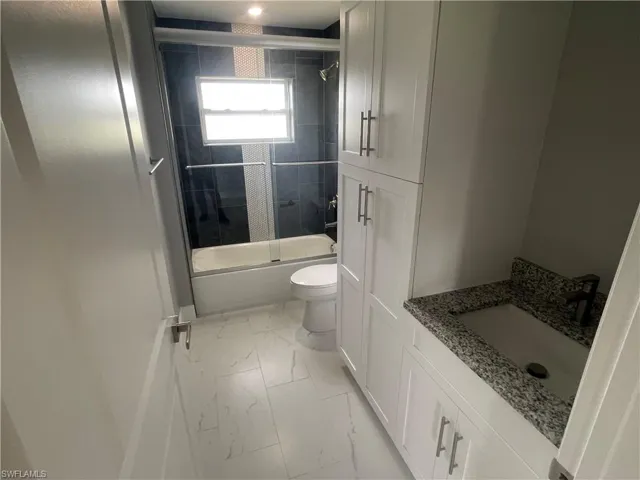 Bathroom with shower / bath combination with glass door, vanity, and light marble finish flooring