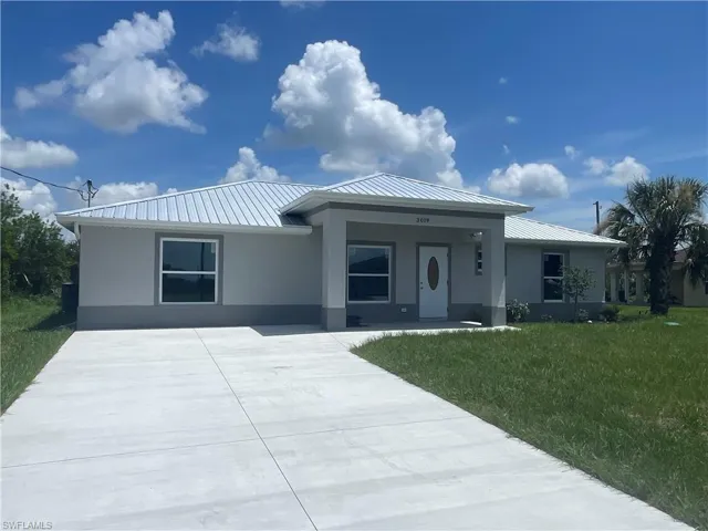 View of front facade featuring a front lawn, stucco siding, concrete driveway, and a metal roof