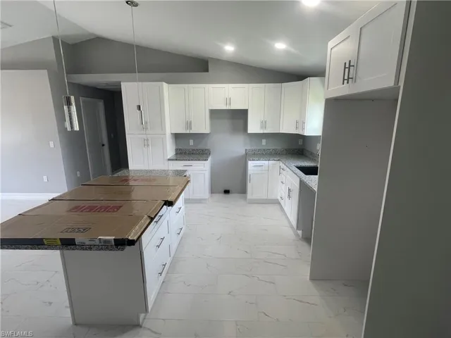 Kitchen with lofted ceiling, white cabinets, light marble finish floors, a center island, and decorative light fixtures