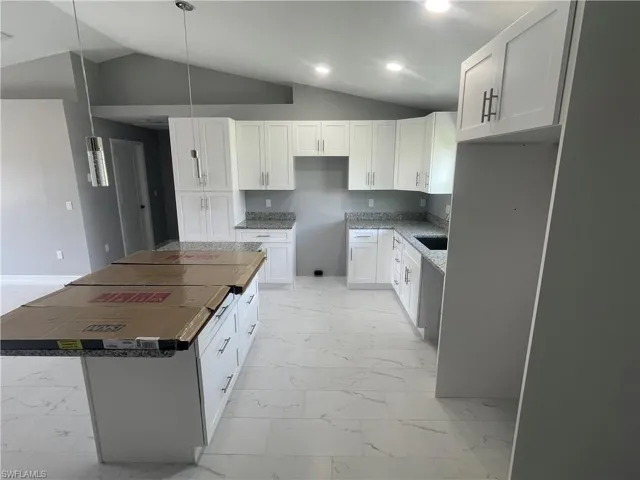 Kitchen featuring vaulted ceiling, white cabinetry, a kitchen island, light marble finish floors, and hanging light fixtures