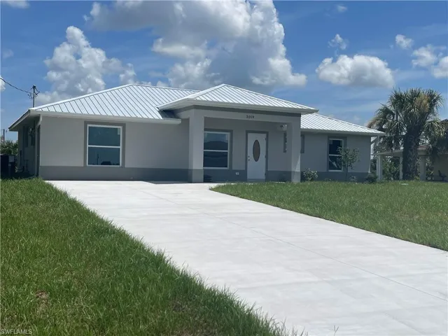 View of front facade featuring stucco siding, a front lawn, a metal roof, and concrete driveway