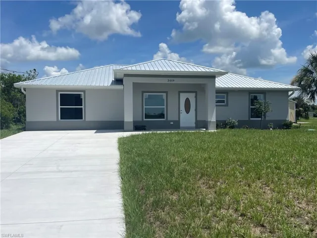 View of front facade featuring a front lawn, stucco siding, a metal roof, and driveway