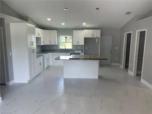 Kitchen featuring lofted ceiling, white cabinets, a kitchen island, pendant lighting, and dark stone counters