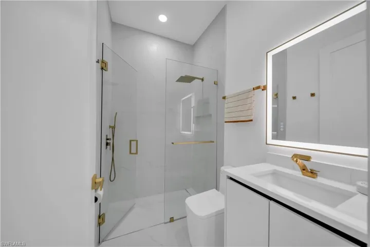 Modern bathroom featuring a frameless glass shower enclosure, a vanity with a rectangular basin, and a backlit mirror
