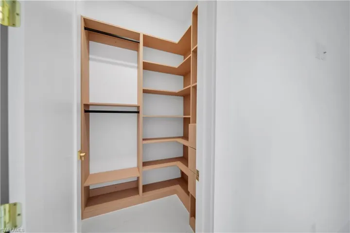 Built-in closet system featuring light wood-finish shelving, multiple hanging rods, and corner storage