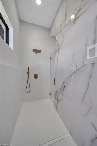 Walk-in shower featuring a rain shower head, hand-held shower fixture, glass enclosure, linear drain, and large format wall tile with veining