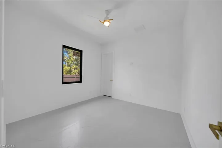 Bright room featuring a single window with dark trim, a white ceiling fan with gold accents, and a white door with a gold handle