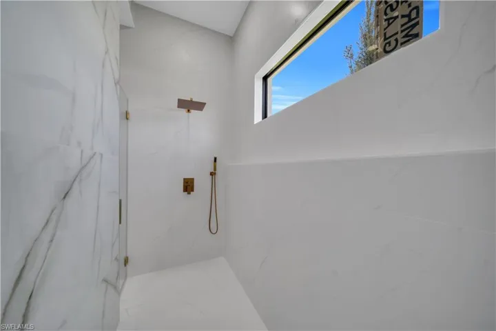 Walk-in shower featuring full-height white tile, a fixed glass panel, bronze-finish fixtures, and a horizontal window