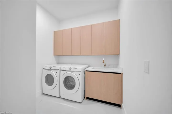 Dedicated utility space featuring light wood-finish cabinetry, a built-in sink with a gold-tone faucet, a white countertop, and clean white walls