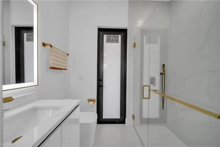 Contemporary bathroom featuring a floating vanity with integrated sink, illuminated mirror, and gold-finish fixtures