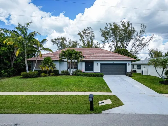Ranch-style home featuring a front yard, driveway, an attached garage, stucco siding, and a tiled roof