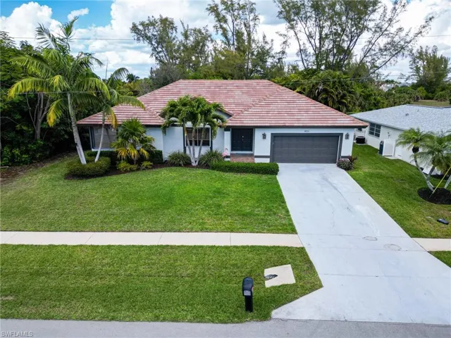 Ranch-style home with a front yard, driveway, a garage, stucco siding, and a tiled roof