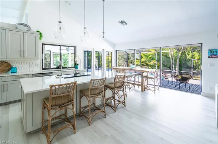 Kitchen with lofted ceiling, backsplash, light stone counters, a kitchen bar, and a kitchen island with sink