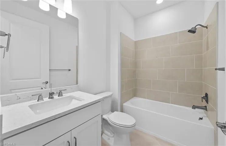 Full bathroom featuring vanity, tiled shower / bath combo, toilet, and tile patterned floors