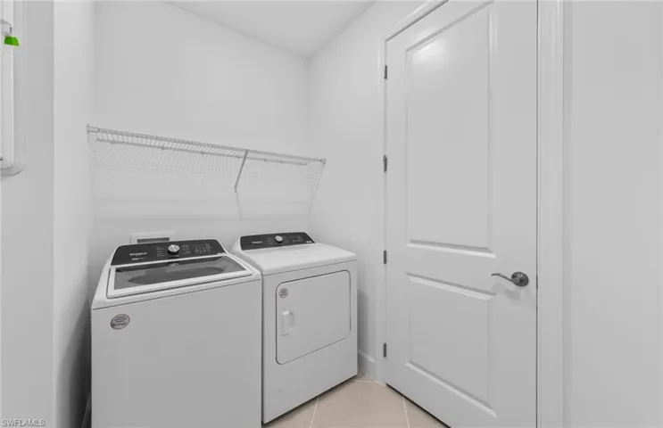 Washroom with light tile patterned flooring and washing machine and clothes dryer