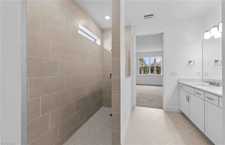 Bathroom with tile patterned flooring, tiled shower, and vanity