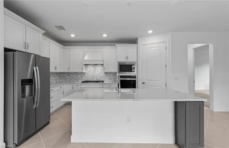 Kitchen featuring custom exhaust hood, light tile patterned floors, an island with sink, and stainless steel appliances