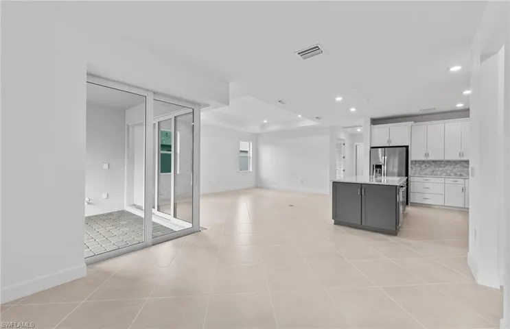 Kitchen featuring white cabinets, backsplash, light tile patterned floors, a kitchen island, and stainless steel refrigerator with ice dispenser