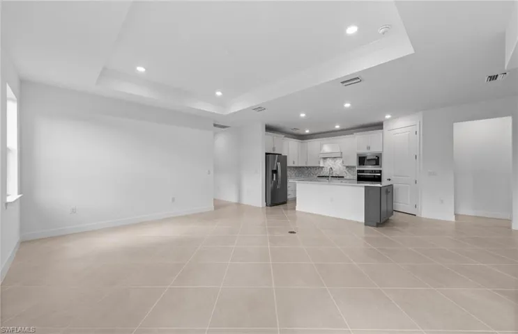 Kitchen featuring stainless steel appliances, backsplash, a center island with sink, and a tray ceiling