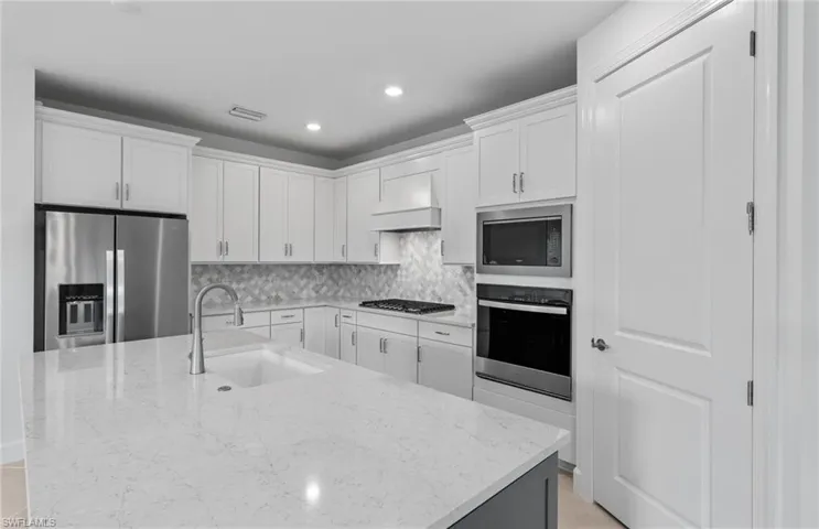 Kitchen featuring stainless steel appliances, white cabinets, sink, decorative backsplash, and custom exhaust hood