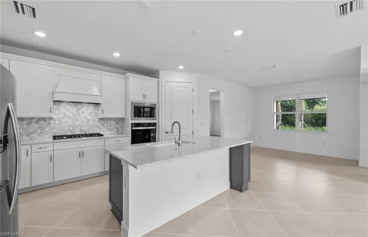 Kitchen featuring light tile patterned flooring, tasteful backsplash, stainless steel appliances, custom exhaust hood, and sink