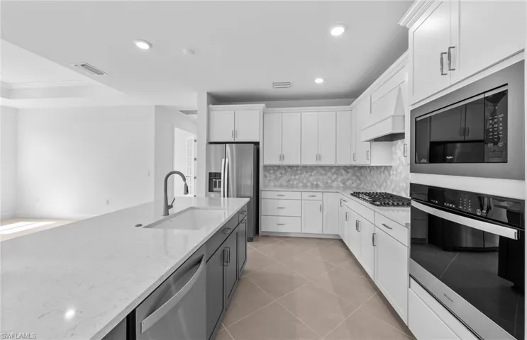 Kitchen with tasteful backsplash, light tile patterned floors, white cabinets, stainless steel appliances, and sink
