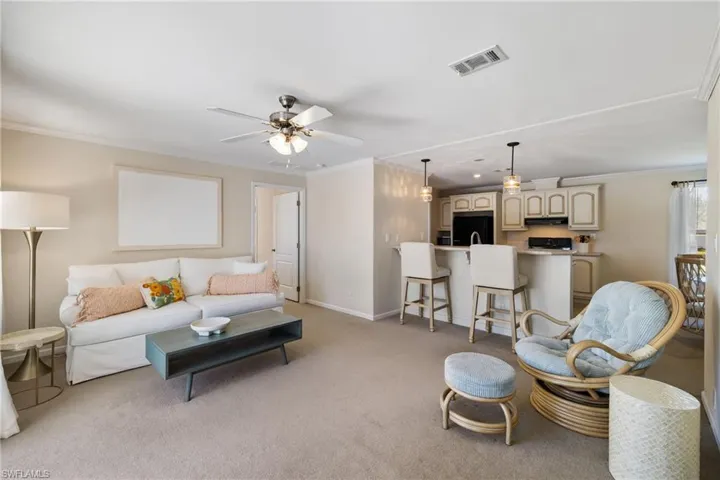 Living room featuring light carpet, baseboards, visible vents, and ornamental molding