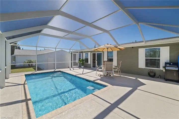 Outdoor pool featuring glass enclosure, an outdoor structure, area for grilling, and a patio