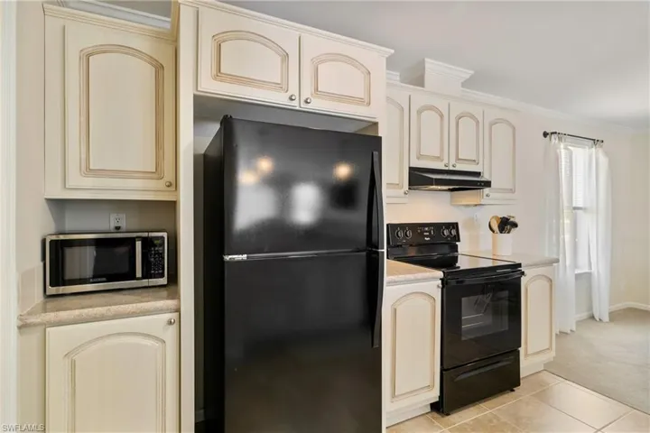 Kitchen featuring light tile patterned floors, light countertops, cream cabinets, under cabinet range hood, and black appliances