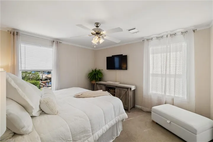 Bedroom with ornamental molding, visible vents, ceiling fan, and light carpet