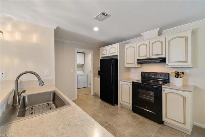 Kitchen with cream cabinetry, washer / clothes dryer, a sink, under cabinet range hood, and black appliances