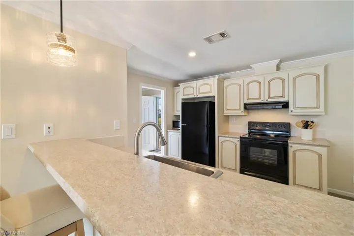 Kitchen featuring visible vents, ornamental molding, cream cabinets, black appliances, and a sink