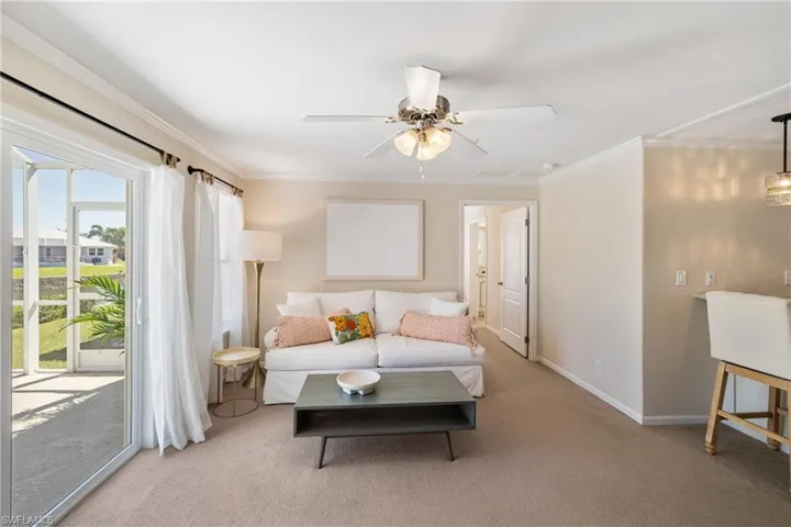 Carpeted living room featuring baseboards, ceiling fan, and crown molding
