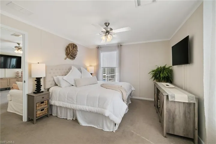 Bedroom featuring a ceiling fan, light colored carpet, visible vents, and crown molding