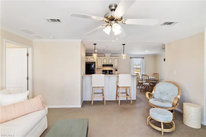 Living room with crown molding, baseboards, visible vents, and light colored carpet