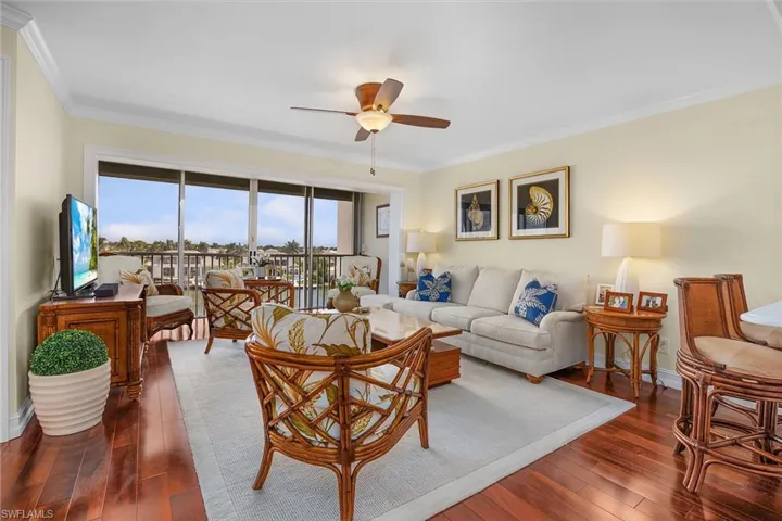 Living room with ornamental molding, dark wood-style flooring, and a ceiling fan