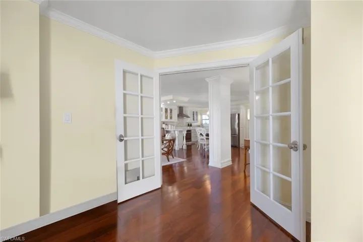 Hall featuring dark wood-type flooring, french doors, ornamental molding, and decorative columns