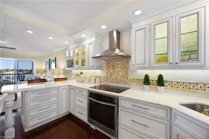 Kitchen with white cabinets, ornamental molding, glass insert cabinets, stainless steel oven, and wall chimney range hood