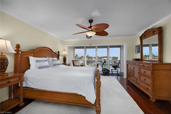 Bedroom with crown molding, access to exterior, dark wood-style flooring, a ceiling fan, and a water view