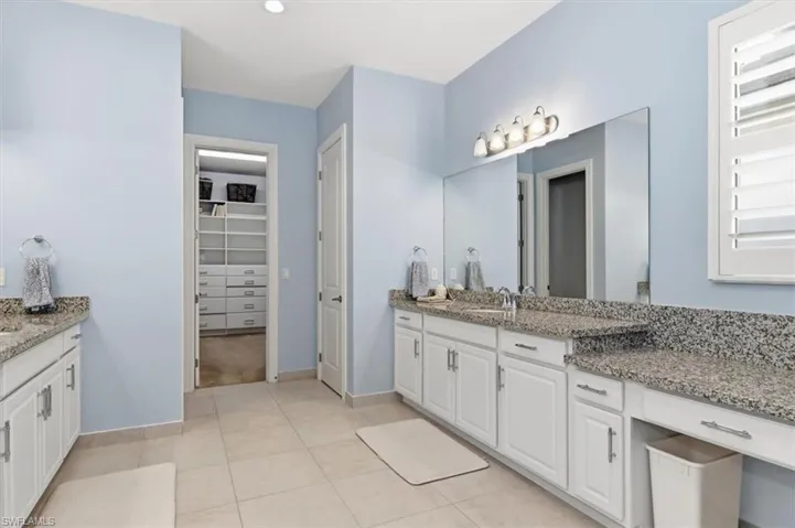 Bathroom with two vanities, a walk in closet, and light tile patterned floors
