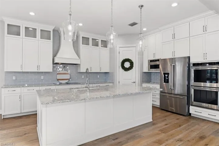 Kitchen featuring stainless steel appliances, white cabinetry, light stone countertops, and light wood finished floors
