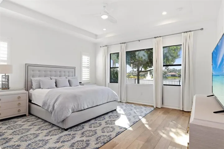 Bedroom with light wood-style floors, a tray ceiling, ceiling fan, and recessed lighting